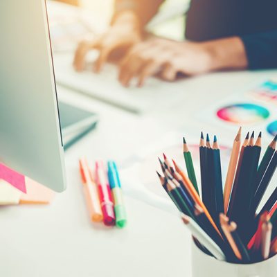 Person with Pantone colour references and pencil crayons on desk with laptop